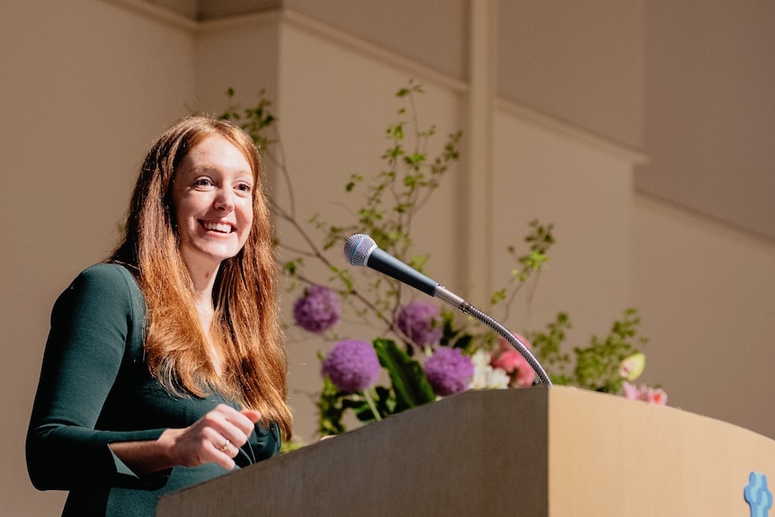 A woman stands at a lecture giving a presentation