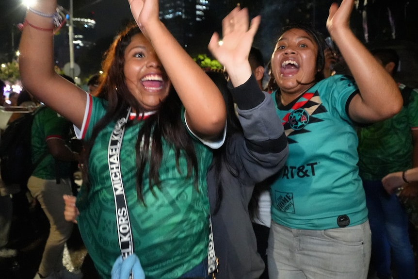 Two women raise their hands in the air and cheer.