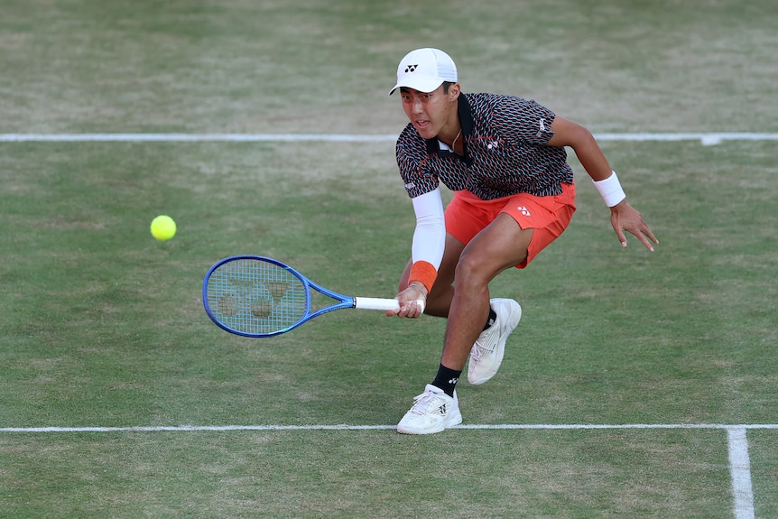 Rinky Hijikata runs and leans forward with his tennis racket low for a hit on the court as the ball approaches.