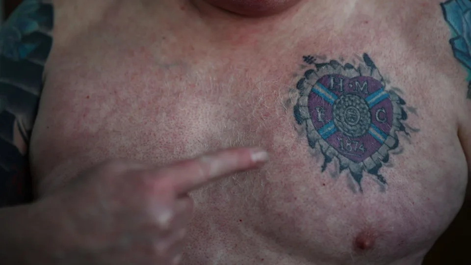 A Hearts fan points to a tattoo of the club's claret crest on his chest.