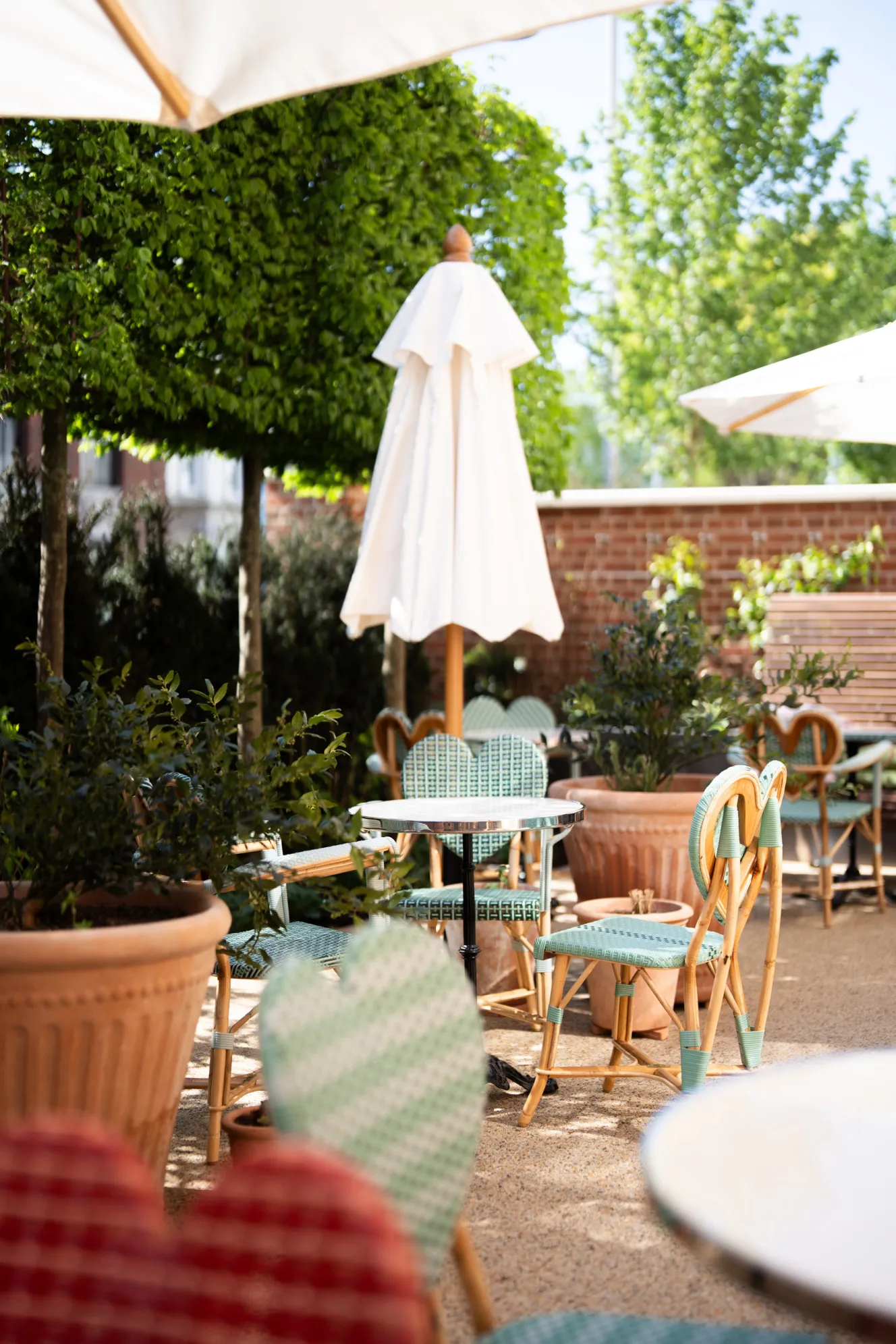 An outdoor patio with light green and white woven chairs and small round tables, shaded by white umbrellas.