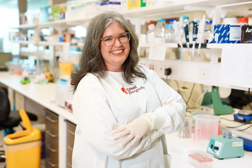 A woman in a white lab coat smiles at the camera.