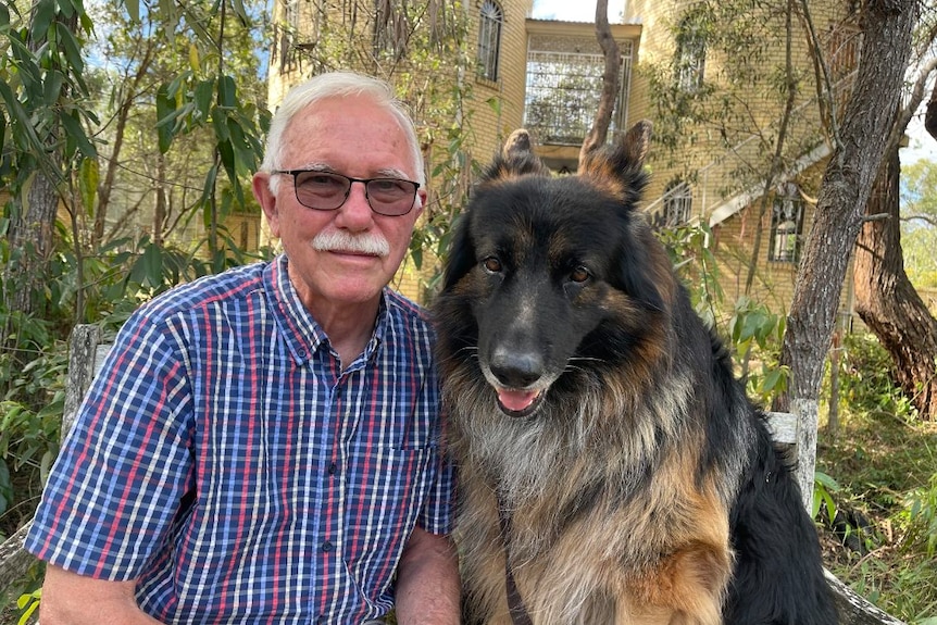 Dr Day sits with his large dog in front of a tree. He is smiling.