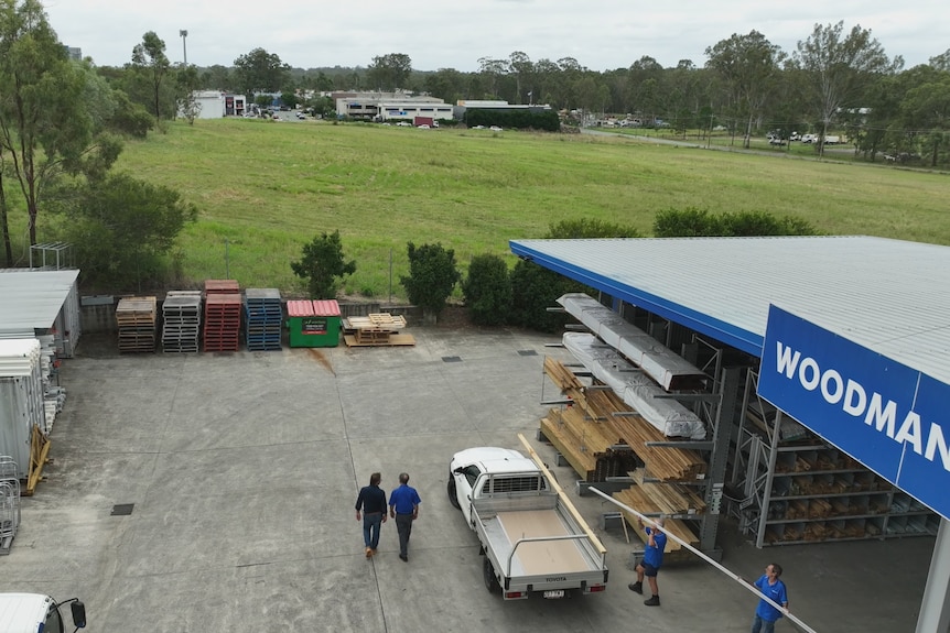 An aerial shot of a large open grass block. In the foreground is a hardware store where pallets and timber is lined up.