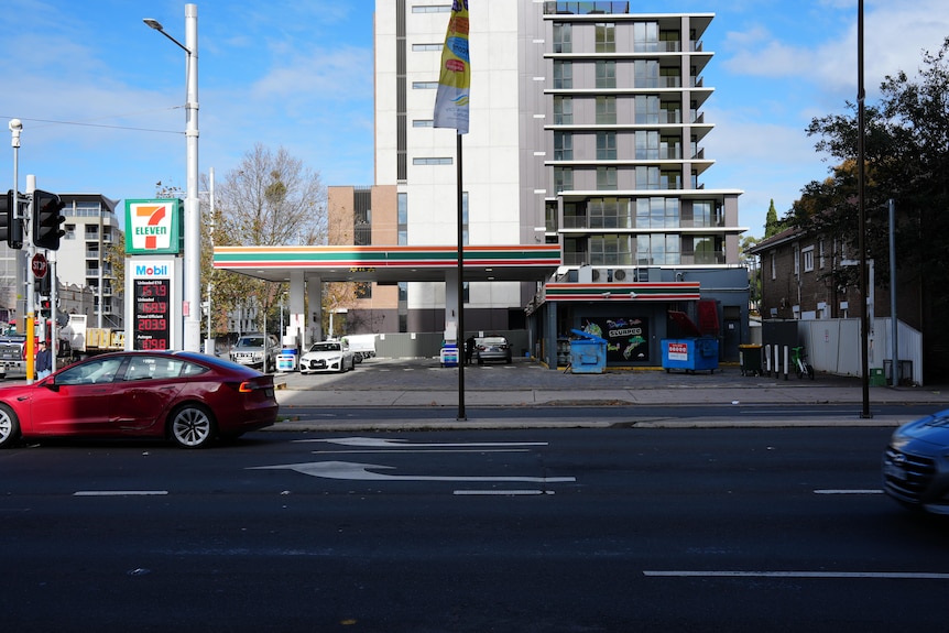 A 7-Eleven petrol station on a city street near a high-rise unit building.