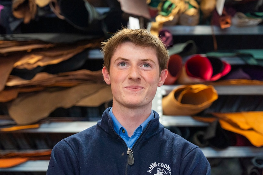 a man in a navy jumper with short hair, holding whips and leather he has made