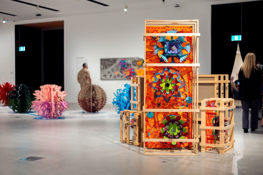 A large sculpture, featuring colourful elements displayed in stacked wooden crates, in an art gallery.