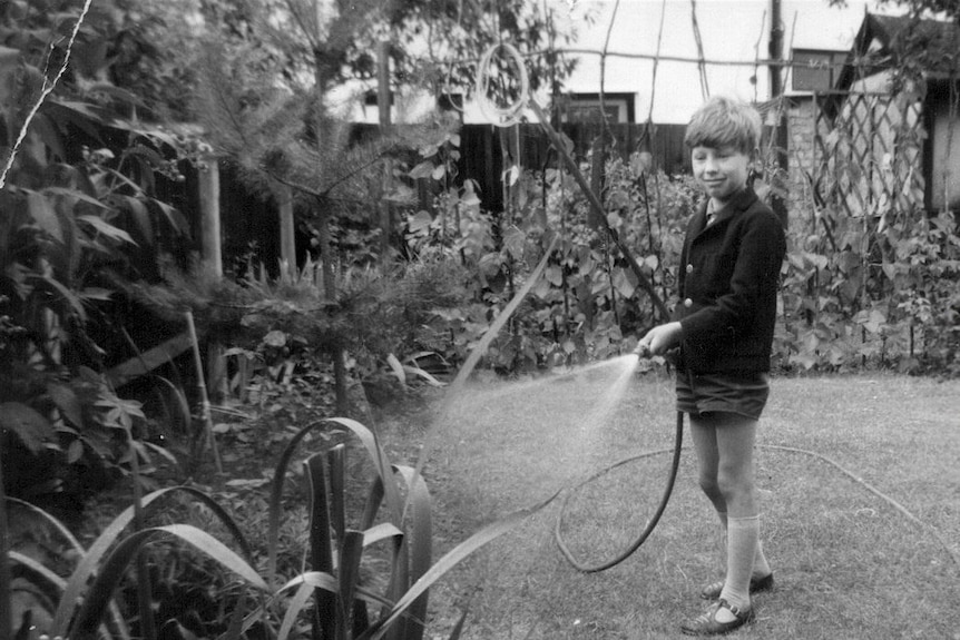 Black-and-white photo of Jerry Coleby-Williams as a child, watering a backyard