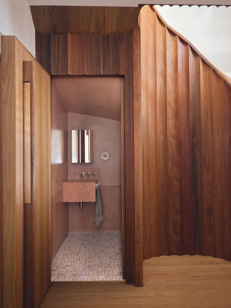 A compact powder room is tucked into the sculptural stair, defined by a soft pink finish.