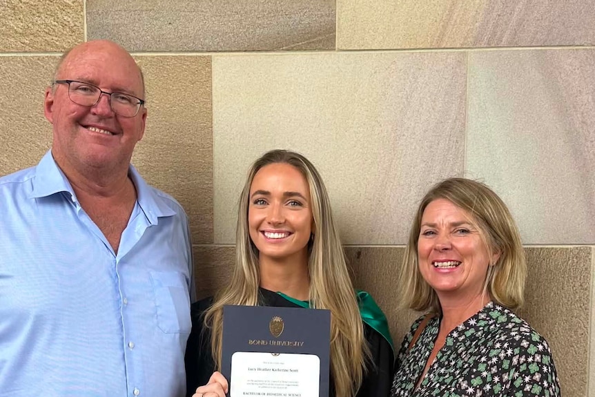Lucy Scott holding her biomedical sciences diploma, standing with her parents on graduation day.