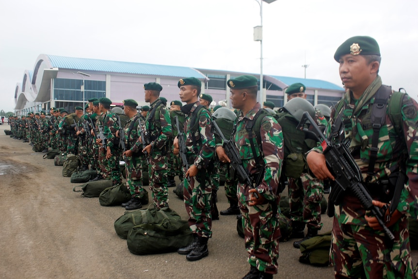 Dozens of Indonesian soldiers in fatigues line up with rifles in hand