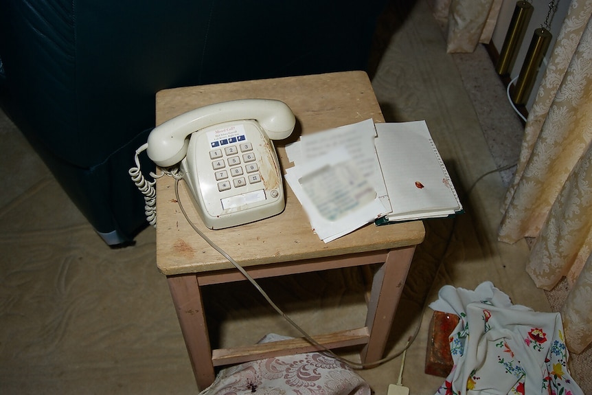 A white landline phone sits on a wooden table with a book next to it. 