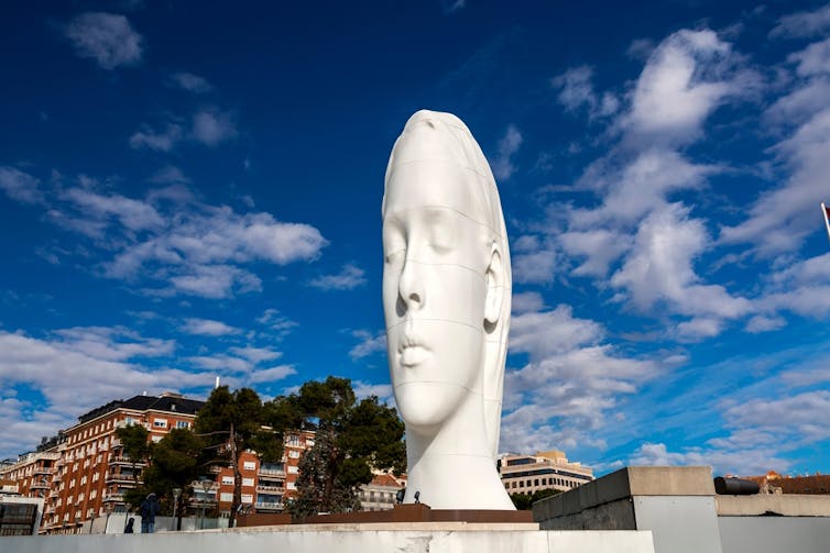 A large sculpture of a woman's head, distorted so that it appears almost flat along the sides.