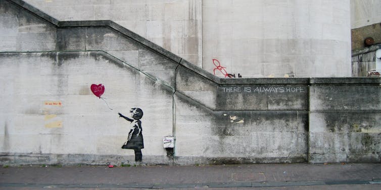 Una niña dibujada en gris sobre una pared clara mientras observa cómo un globo con forma de corazón se escapa.