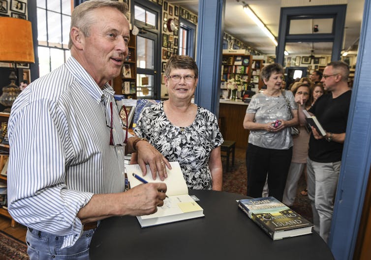 a man signing a book for a woman