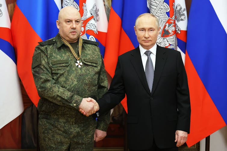 a man with a medal in uniform shaking hands with Vladimir Putin