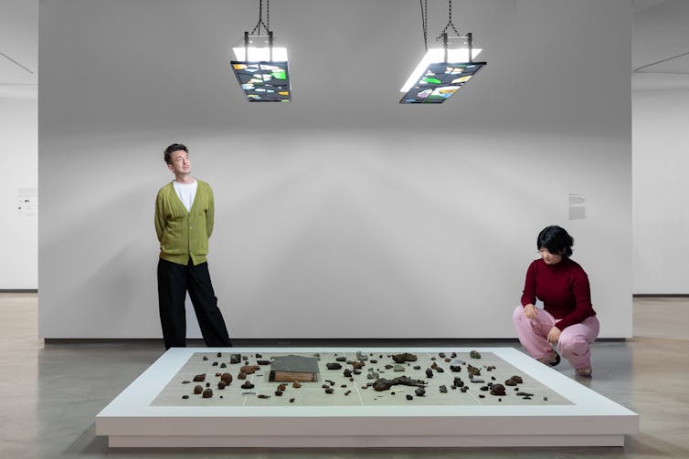 Two people look at a low table with black rocks.