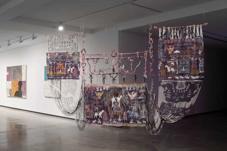 Three weavings hang in a gallery.