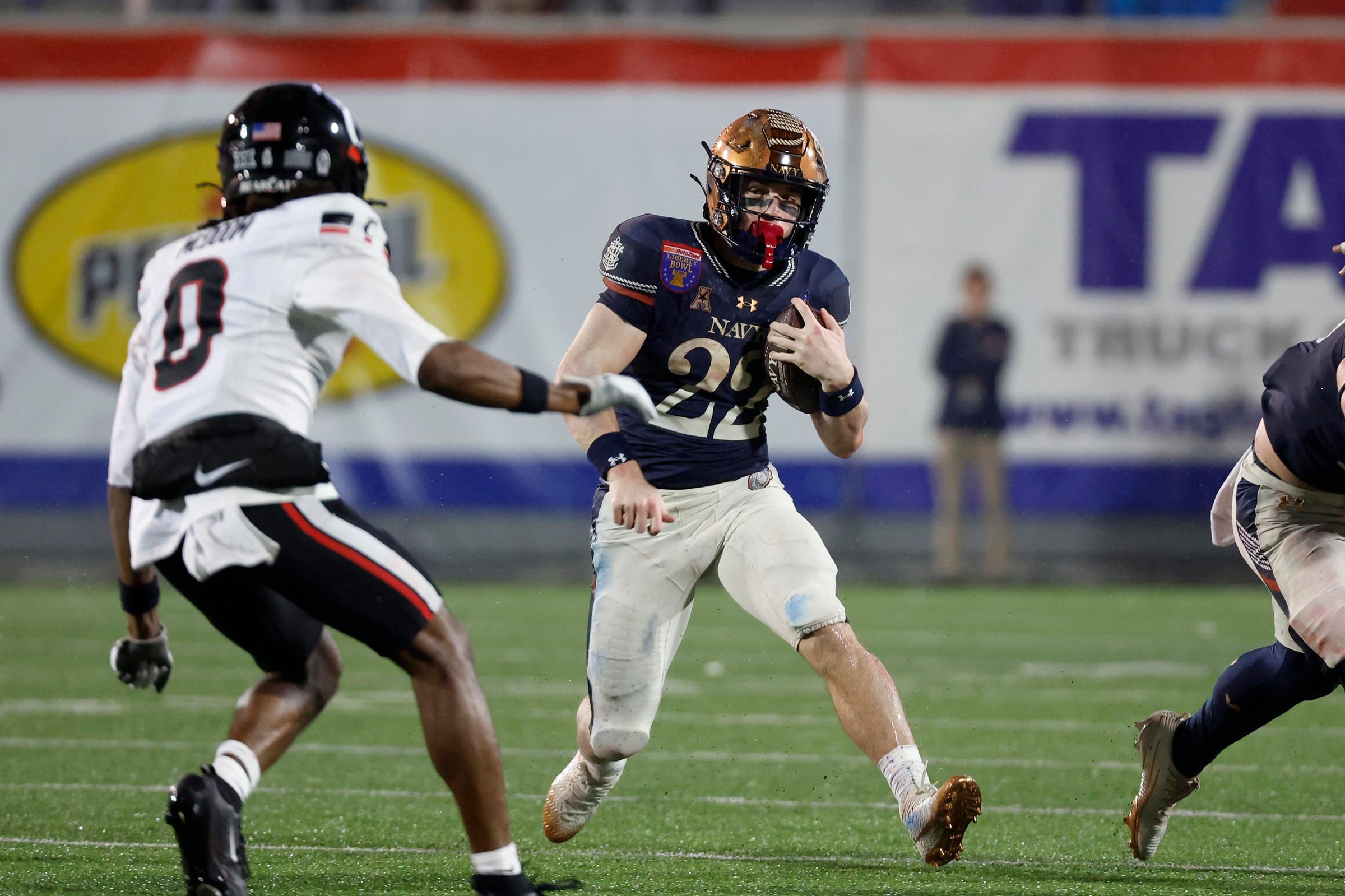 MEMPHIS, TN - JANUARY 02: Navy Midshipmen running back Eli Heidenreich (22) runs the ball as Cincinnati Bearcats cornerback Matthew McDoom (0) looks to make a tackle during the AutoZone Liberty Bowl, January 2, 2026, at Simmons Bank Liberty Stadium in Memphis, Tennessee. (Photo by Matthew Maxey/Icon Sportswire via Getty Images)