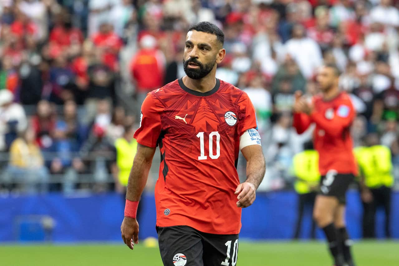 An Egyptian football player in a red jersey on a pitch, looking towards his right