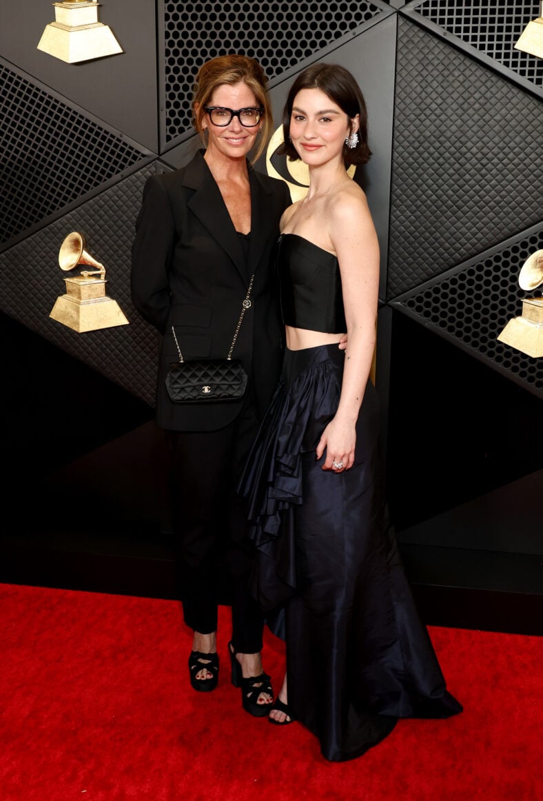 Gracie Abrams and her mom Katie McGrath pose together on the red carpet at the Grammys, standing in front of the event backdrop.