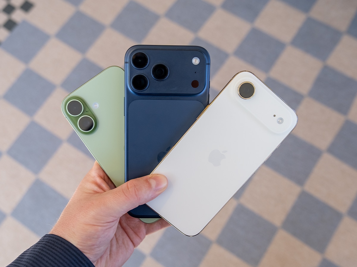 iPhone 17 lineup in hand, featuring green, blue, and white models on a checkered floor background.
