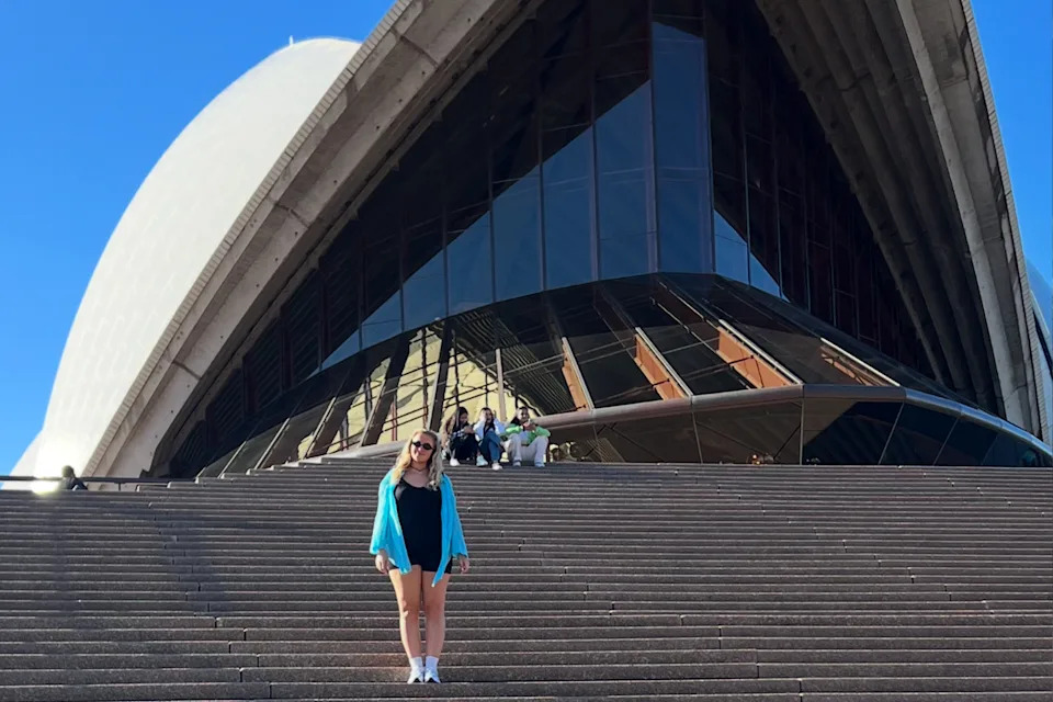 Rebecca standing on the steps beneath the Sydney Opera House.