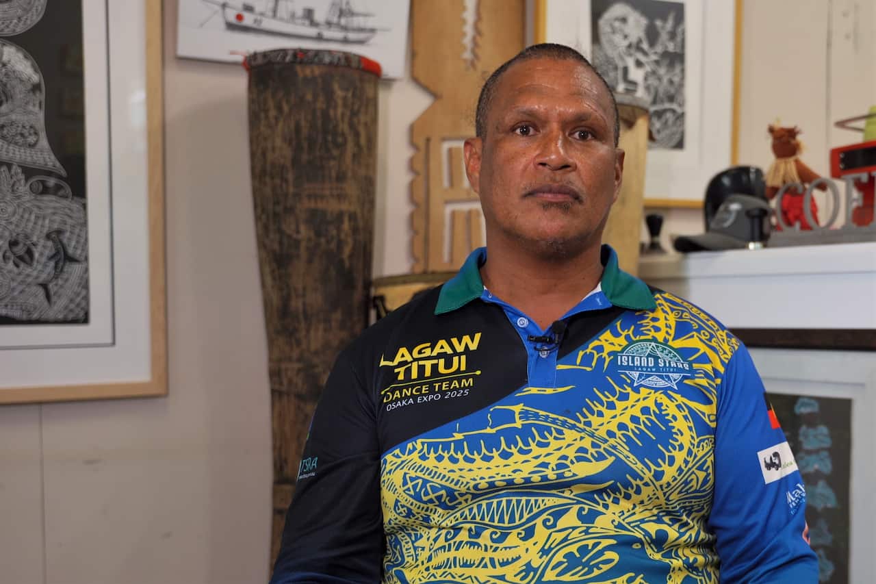 A man in a blue-and-yellow print-patterned polo shirt is sitting in a room.