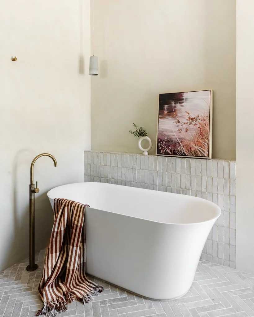 Bathroom with limestone finish walls herringbone tile flooring and a freestanding bath.
