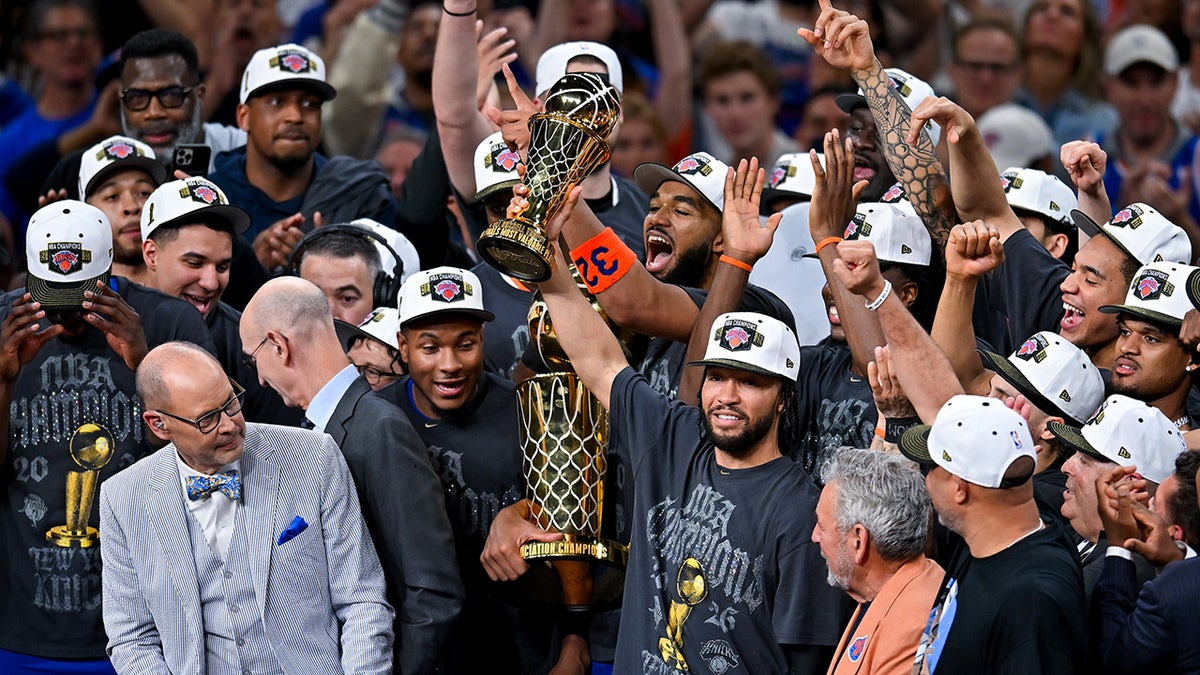 New York Knicks players celebrating with Larry O'Brien Championship Trophy on basketball court.