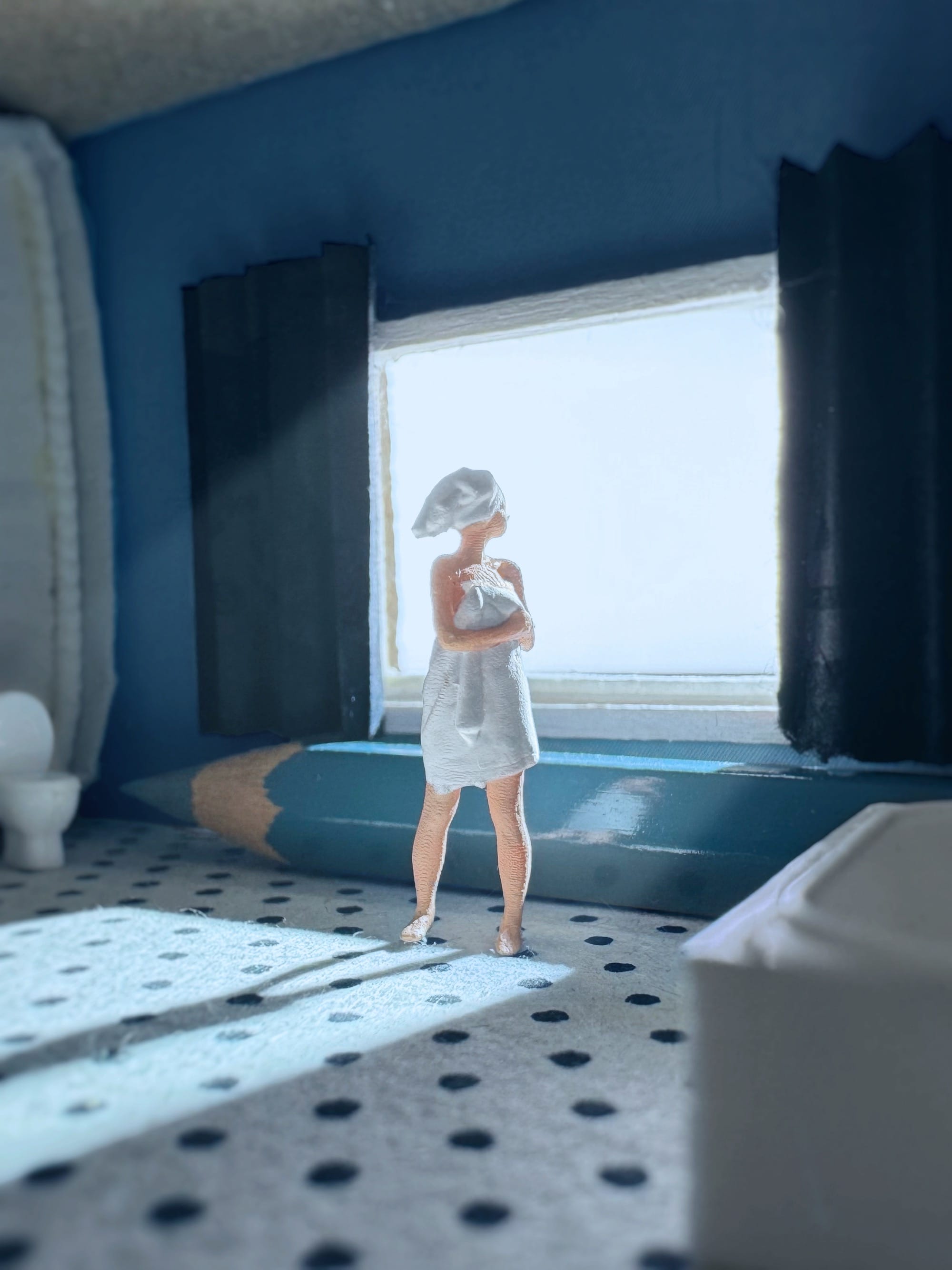 a photograph of a miniature tableau by Derrick Lin of a woman wearing towels, peering out of a large window in front of a huge pencil