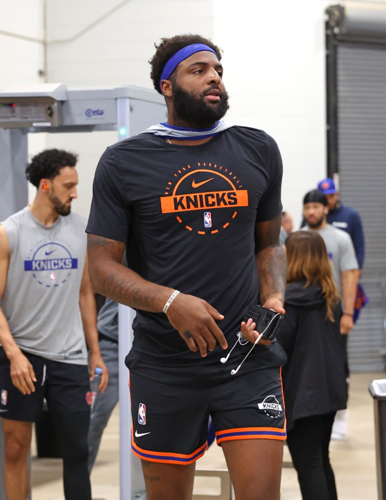 New York Knicks center Mitchell Robinson, wearing a blue headband, black t-shirt, and shorts with orange and blue stripes, arrives at the arena for media day.