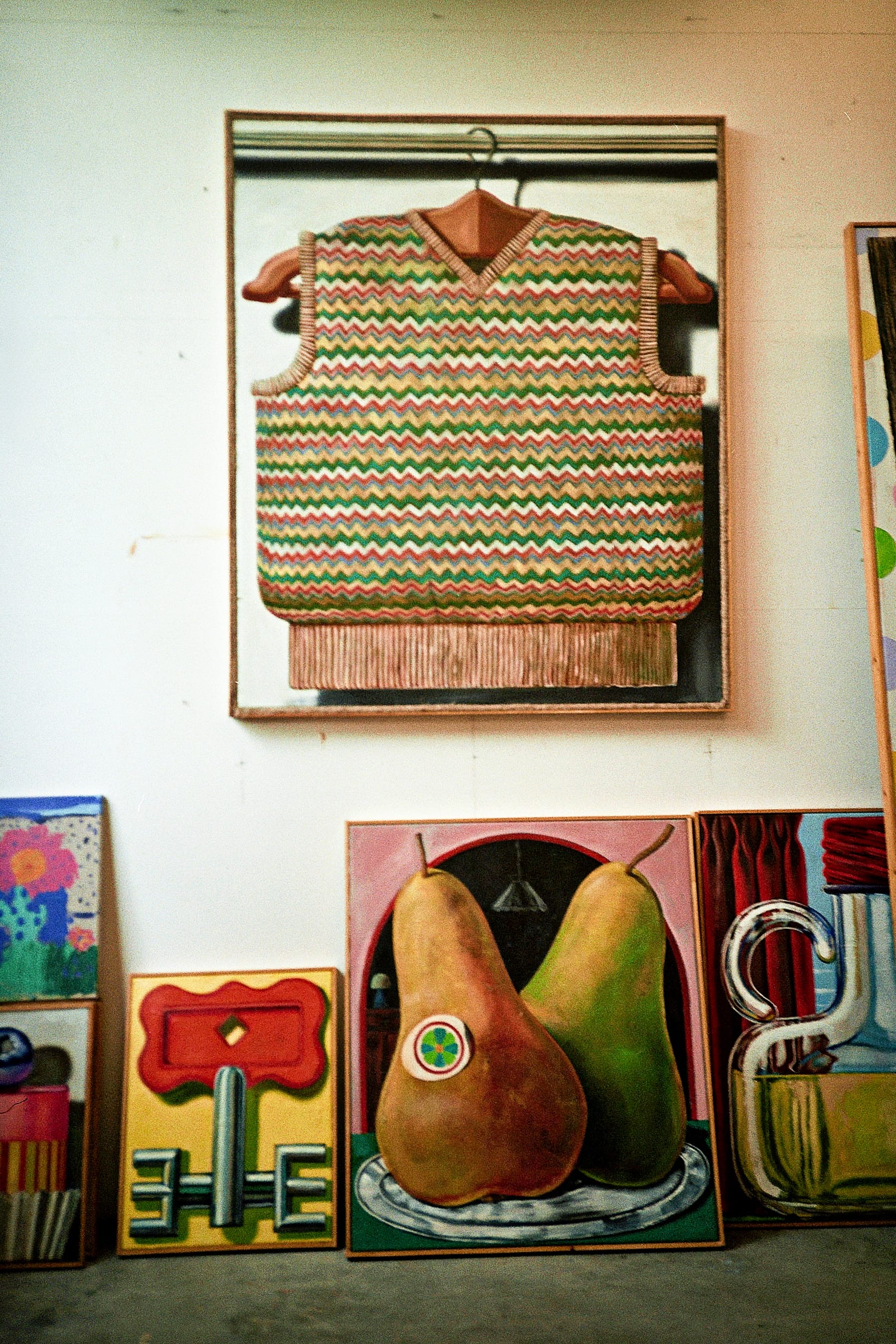 a glimpse of kristof santy's studio with a sweater painting on the wall and fruit works resting on the floor below