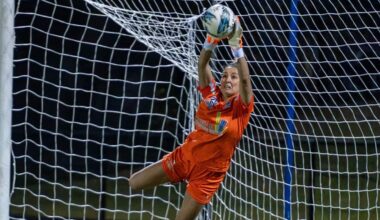 A woman in an orange football uniform catches a ball mid-air