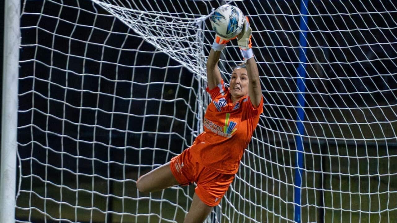 A woman in an orange football uniform catches a ball mid-air