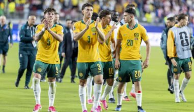 Australian football players in green and gold jerseys clapping a football pitch.