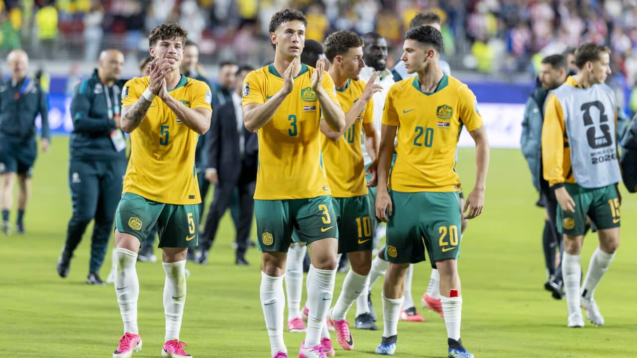 Australian football players in green and gold jerseys clapping a football pitch.