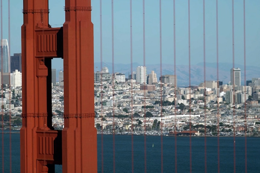 A red coloured bridge over a harbour with a city in the background