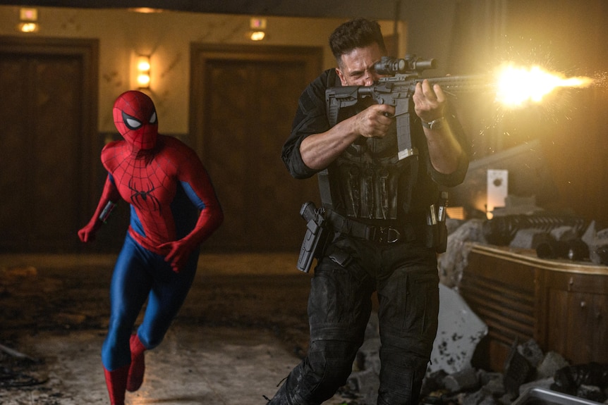 Spiderman walks next to the punisher who is shooting a gun