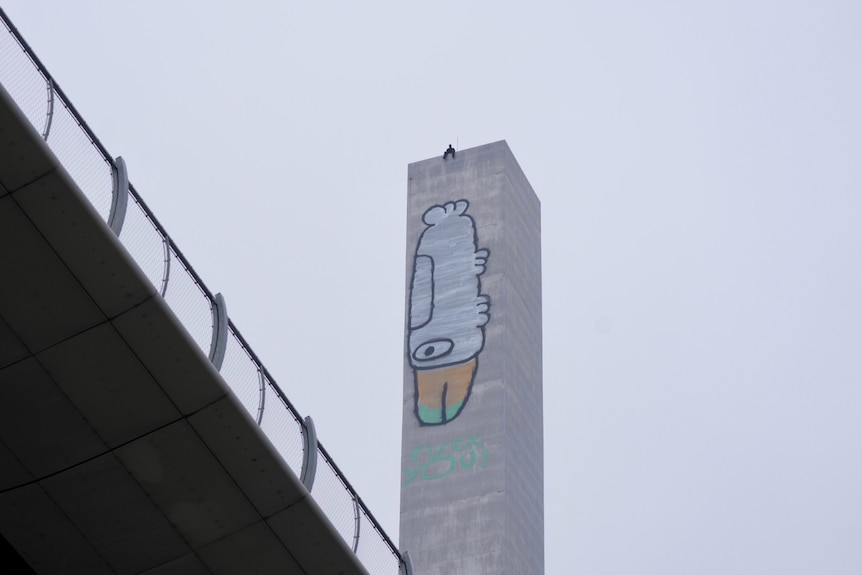 Man sits at the top of the Bolte Bridge pylon with a chicken illustration.