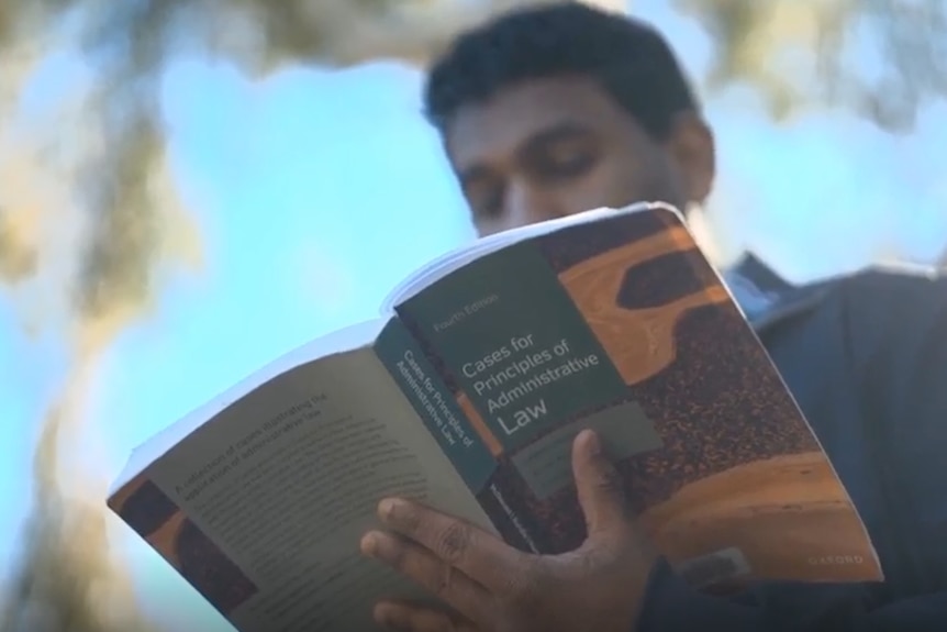 man is reading a legal studies textbook. he is outside.
