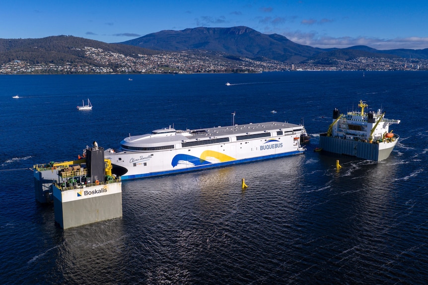 A large ferry being moved onto larger transport ship.