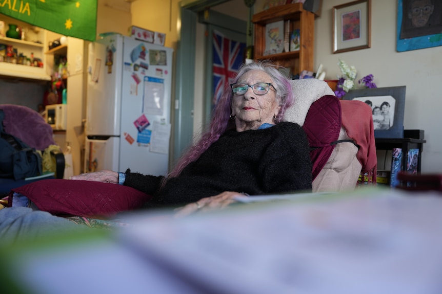 An old lady sits in an armchair and reflects on the future in cluttered apartment