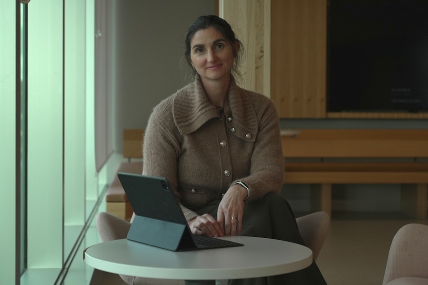 Maria Yanotti sits at a table by a window, hunched over her Ipad, smiling.