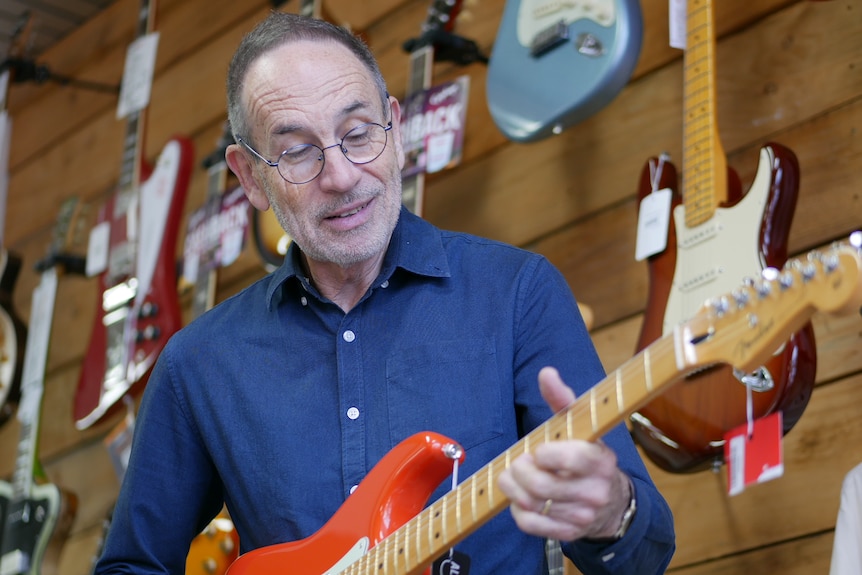 Dale Alison smiling as he looks down at his guitar in the middle of his music shop
