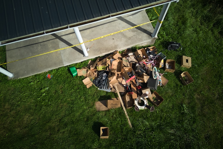 A drone image shows debris including cardboard boxes strewn across a lawn, a concrete patio can be seen in top left corner