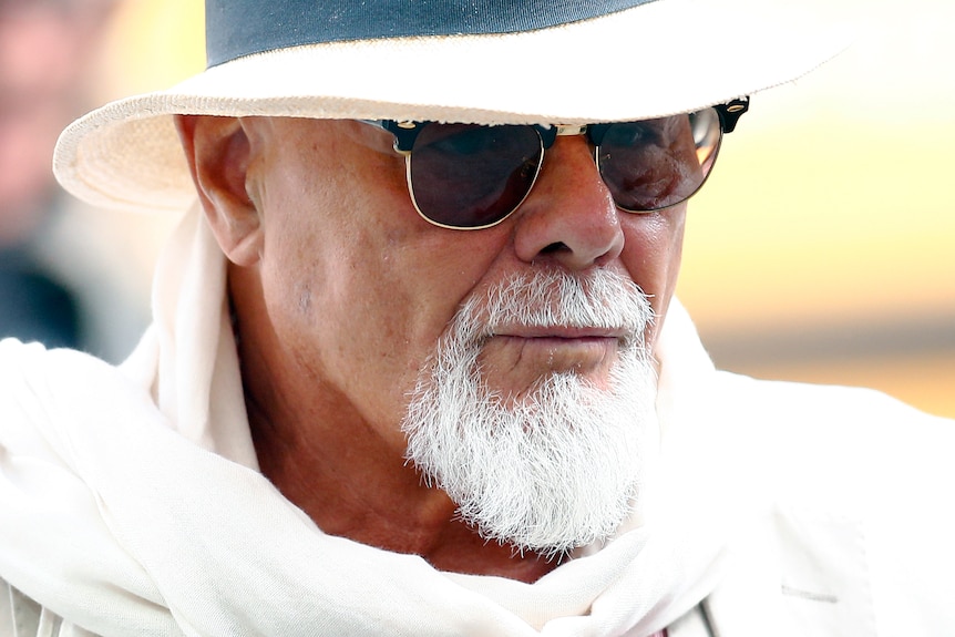 A man with a white goatee wearing sunglasses and a white hat.