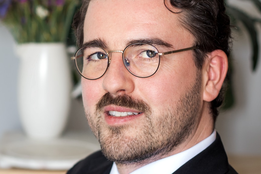 Tom Hercules Davies with reading glasses, brown hair, wearing a suit