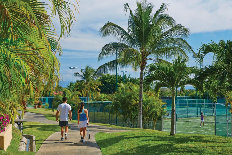 Four Seasons Resort Punta Mita people walking on a path towards tennis courts surrounded by palm trees.