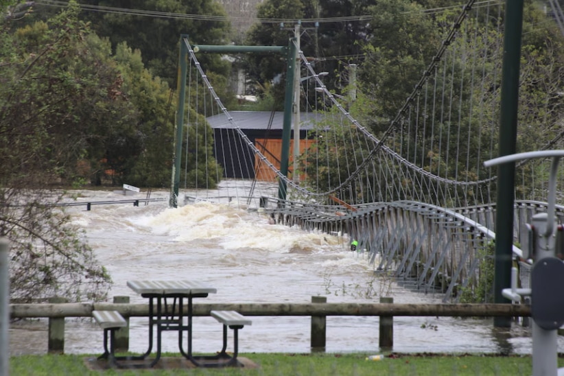 a steel grey bridge is lashed by a rising river with water overflowing onto the bridge